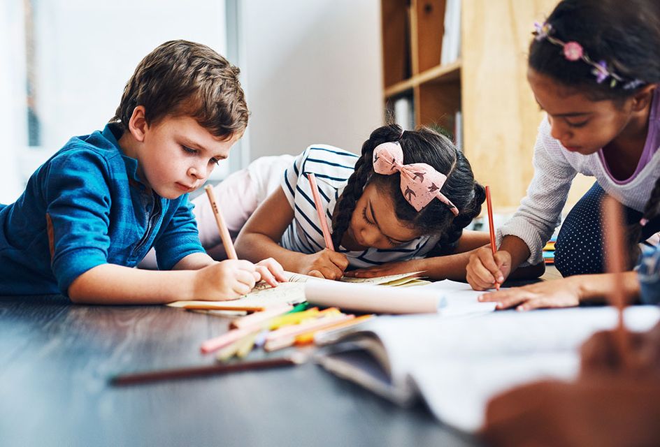 A group of children writing and drawing in notebooks with coloured pencils.