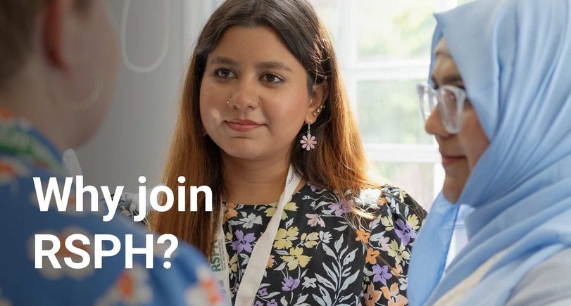 Two young women listen to another woman who is talking in the foreground. They are both wearing RSPH lanyards.