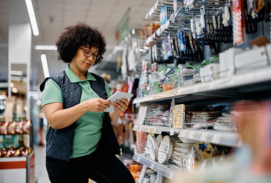 A woman with curly hair and glasses looks at a tablet while working in a hardware shop.
