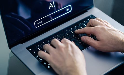 A close-up of a person typing on a laptop. The screen shows a heading that reads 'AI', with a search bar underneath in which the person has started typing 'Create a'