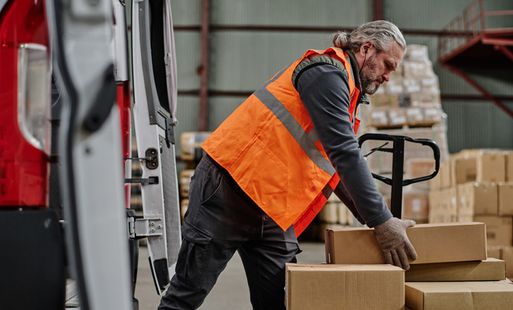 A man in a high-vis jacket lifting a box in a warehouse.