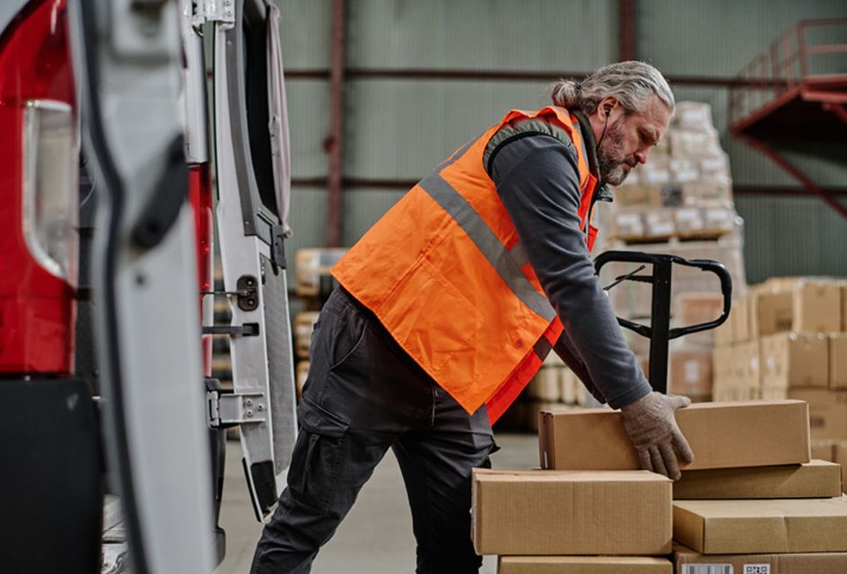 A man in a high-vis jacket lifting a box in a warehouse.
