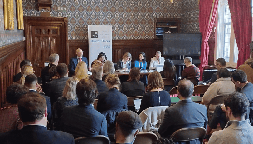 Panel discussion in a room in the houses of parliament with patterned wallpaper and red curtains.