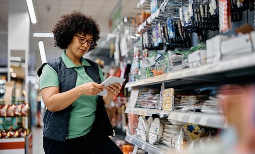 A retail worker in a supermarket looks at an item from the shelf.