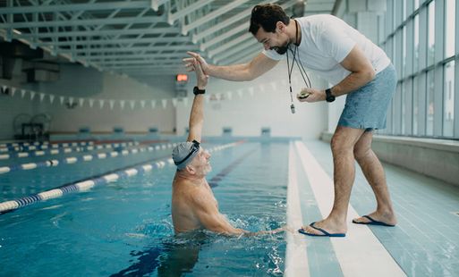 A man in a swimming pool high-fiving his coach, who stands on the side of the pool.