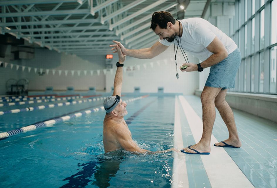 A man in a swimming pool high-fiving his coach, who stands on the side of the pool.