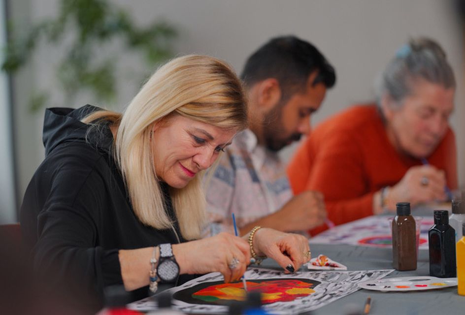 A white woman with blonde hair painting and smiling with a group.